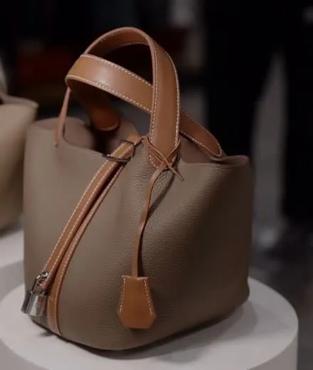 Close view of the taupe pebbled leather, contrast-stitched tan handles, padlock and clochette