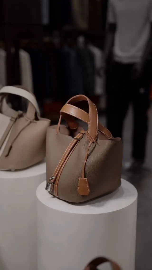 Leather bucket bags with tan handles on white plinths in the store